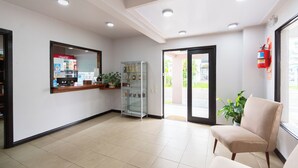 Een receptiegedeelte met een Coca-Cola koelkast, een glazen vitrine, een beige fauteuil en een rode brandblusser.