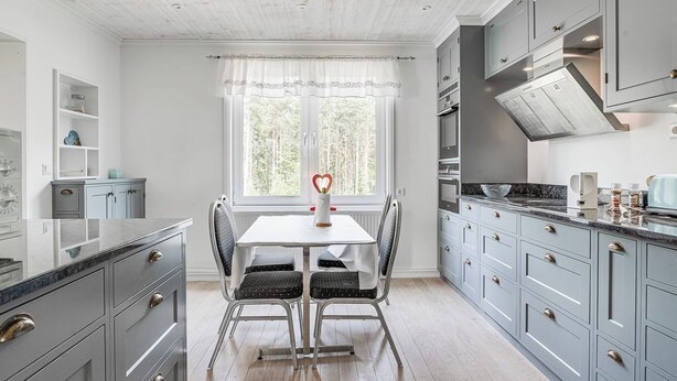 Een moderne keuken met grijze kastjes, een witte tafel en een raam met uitzicht op bomen.