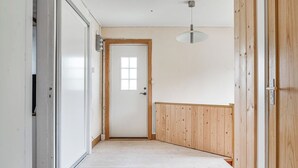 Een gang met een houten vloer, een witte deur met raam, en een plafondlamp.