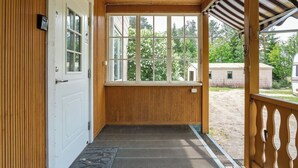 Een overdekte veranda met een houten vloer, een witte deur en een groot raam.