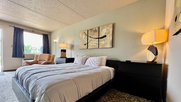 A hotel room with a large bed, a chair, a desk, and a lamp. - Downtown CF Studio - Free Gated Parking! 520 (Cedar Falls)