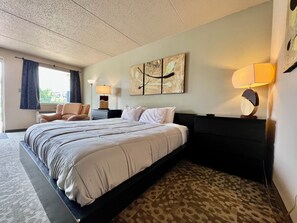 Ein Hotelzimmer mit einem großen Bett, einem Sessel, einem Schreibtisch und einer Lampe.