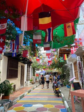 Experience the vibrant street scene with its eclectic mix of international flags, colorful tiles, and lush greenery.