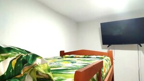Ein Einzelbett mit farbenfroher Bettdecke, ein an der Wand befestigter Fernseher und eine schlichte weiße Wand.