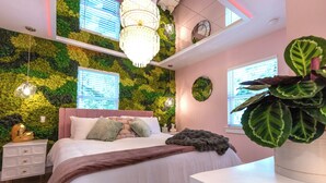 Een slaapkamer met een groene wand, een bed met witte beddengoed, een kroonluchter en een grote plant.
