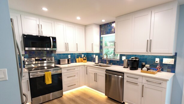 Een moderne keuken met witte kasten, roestvrijstalen apparatuur en een blauwe tegelachterwand.