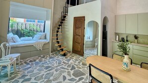 A spacious room with a stone floor, a wooden ceiling, a built-in bench with cushions, a dining table with chairs, and a staircase leading to an upper level. - Atelier Lumi - @_lumicollection (Miami)
