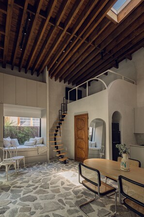 A spacious room with a stone floor, a wooden ceiling, a staircase, and a dining area with a table and chairs. - Atelier Lumi @_lumicollection (Miami)