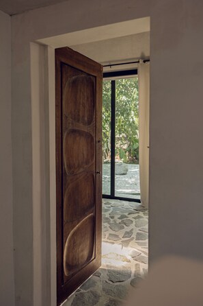 A wooden door leading to a stone-tiled patio with a view of greenery. - Atelier Lumi @_lumicollection (Miami)