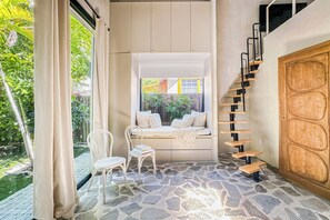 A room with a stone floor, a wooden door, a white bench with cushions, and a white chair. - Atelier Lumi - @_lumicollection (Miami)
