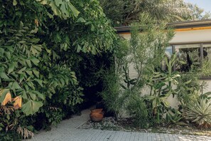 A garden pathway leading to a building with a large window. - Atelier Lumi - @_lumicollection (Miami)