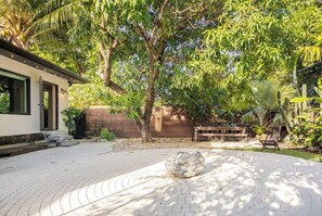 A courtyard with a paved area, a wooden bench, and a large tree. - Atelier Lumi - @_lumicollection (Miami)