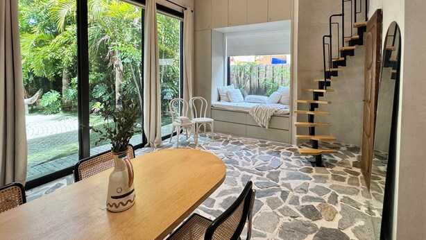 A room with a stone floor, a wooden table, a white sofa, and a staircase. - Atelier Lumi - @_lumicollection (Miami)