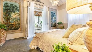 Une chambre à coucher avec un grand lit, un lustre et une vue sur un jardin, visible à travers une porte ouverte.
