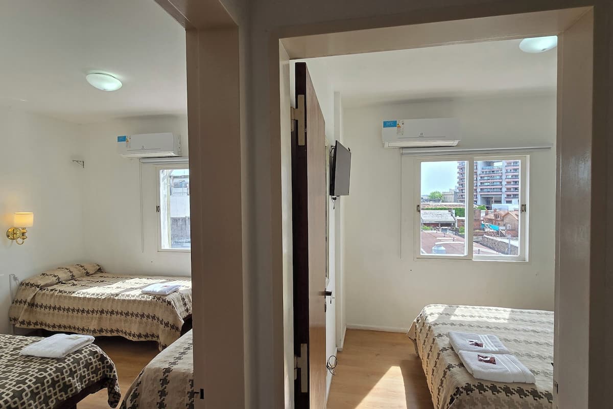 Ein Hotelzimmer mit zwei Betten, einem Fernseher und einem Fenster mit Blick auf Gebäude.