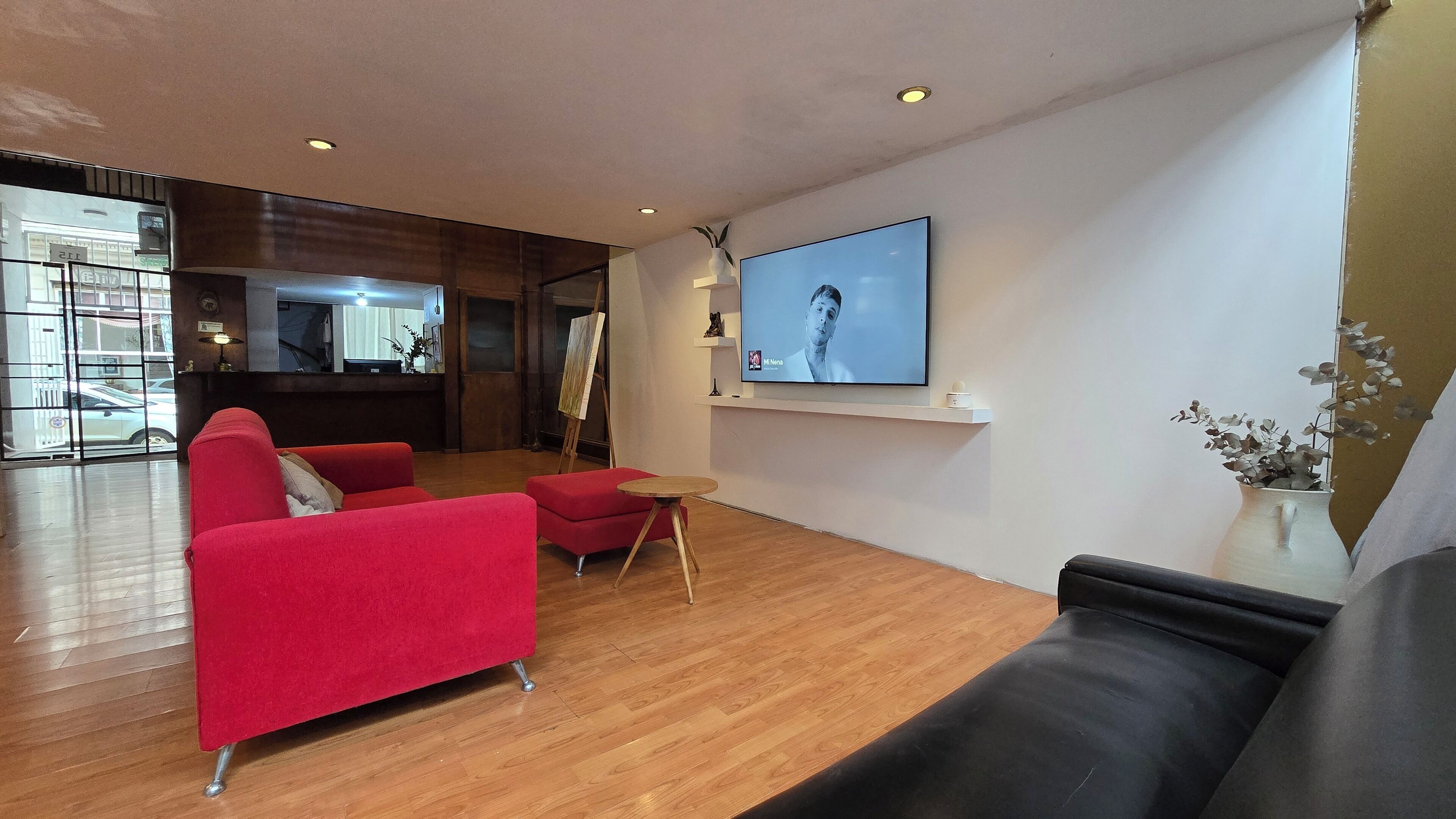A modern living room with a red sofa, a black sofa, and a wooden coffee table. There is a flat-screen TV mounted on the wall, and a potted plant on a side table.