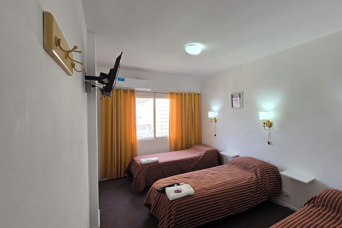 Ein Hotelzimmer mit zwei Einzelbetten, einem Fenster mit gelben Vorhängen, einem Deckenventilator und Wandleuchten.