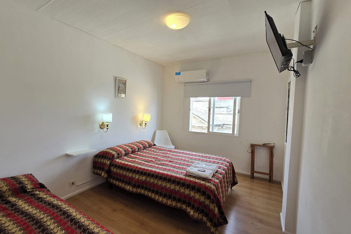 Ein Zimmer mit zwei Betten, einem Fenster, einer Klimaanlage und einem an der Wand befestigten Fernseher.