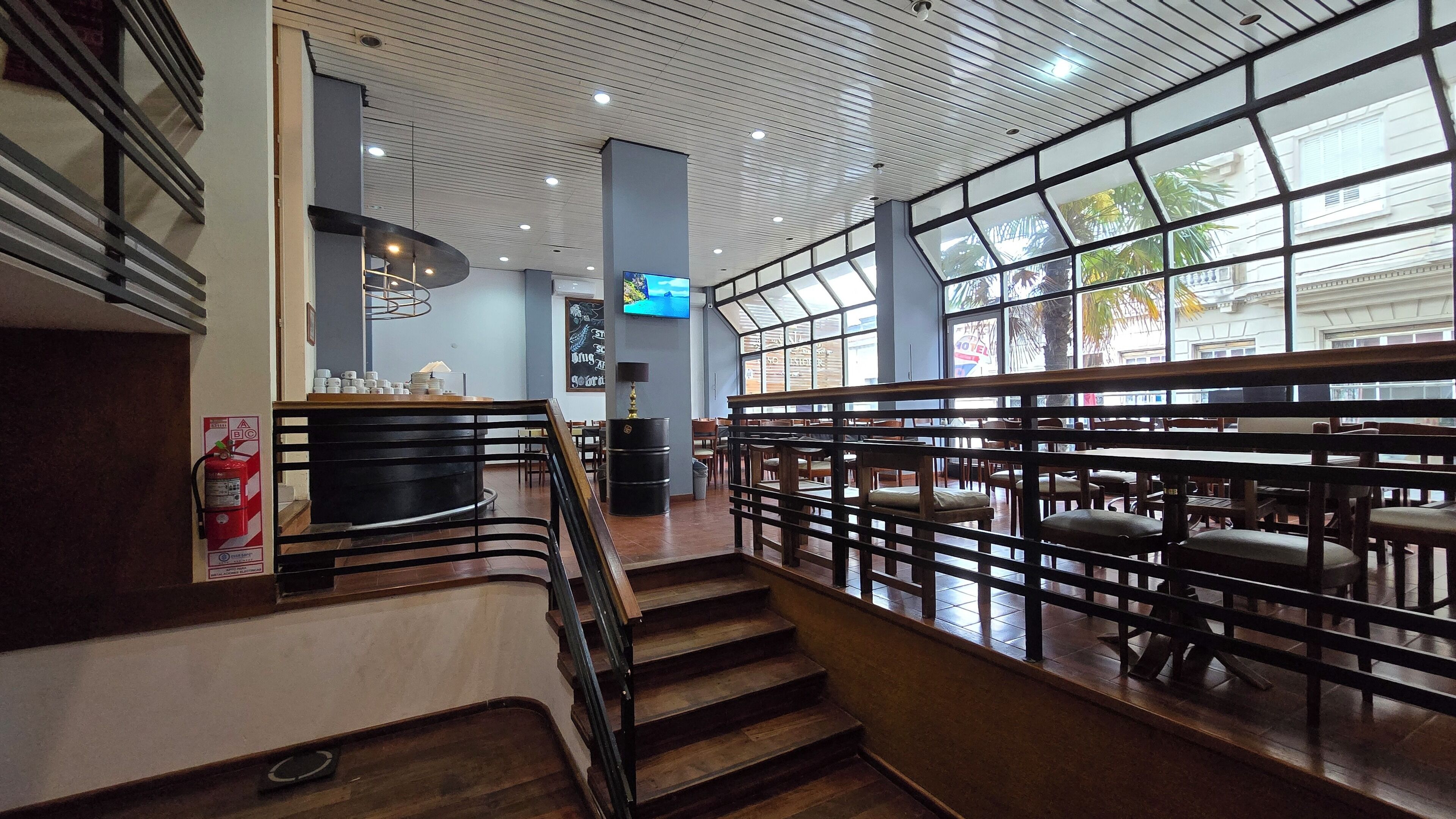 A spacious indoor area with a staircase, wooden railings, and a seating area with tables and chairs.
