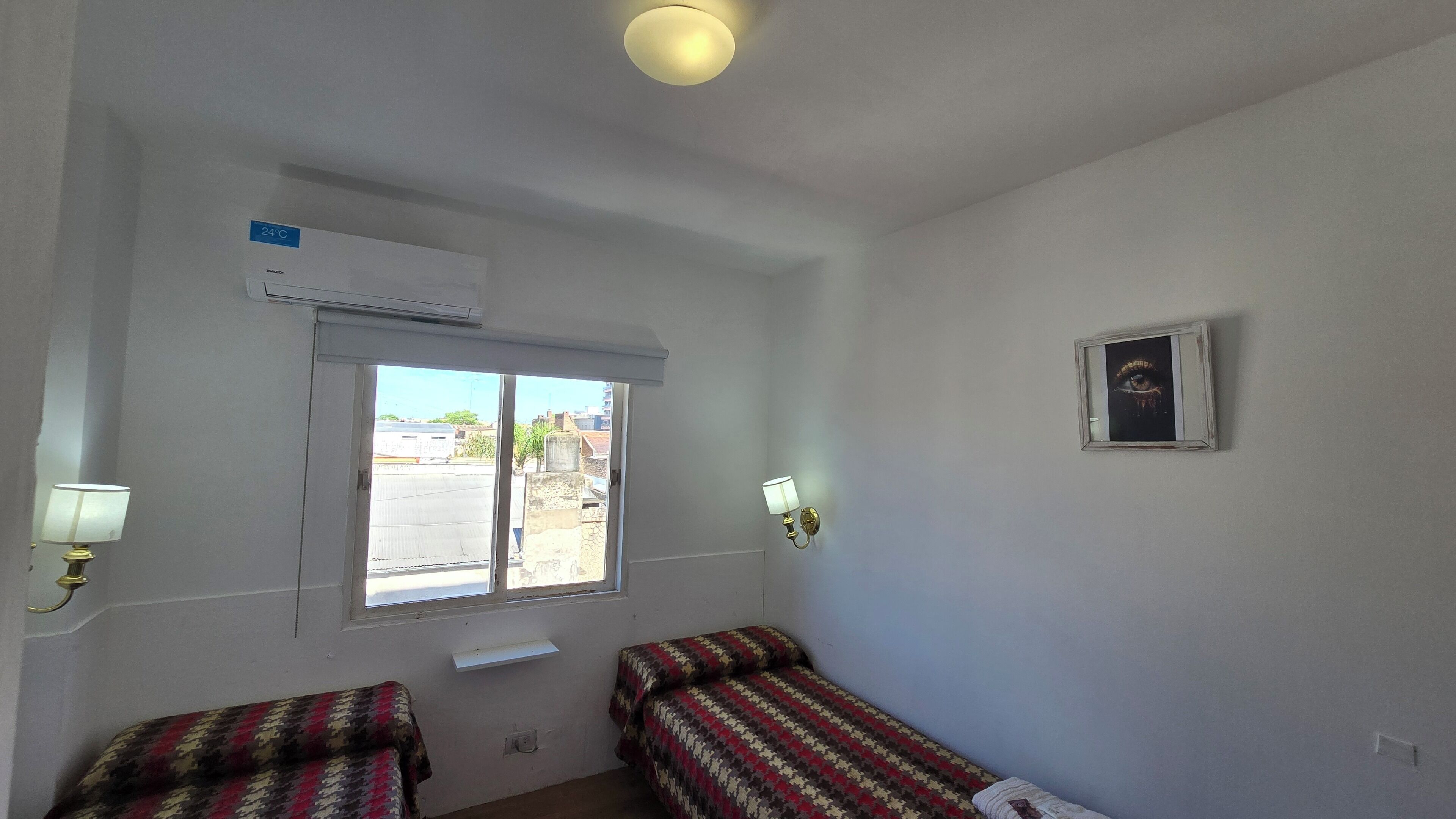 A room with two beds, a window, an air conditioner, and a wall-mounted picture frame.