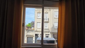 Une vue à travers une fenêtre, à travers un rideau, qui révèle un immeuble doté de nombreuses fenêtres et de balcons.