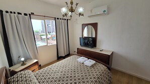 Une chambre à coucher comprenant un lit, une télévision, une commode, un miroir, une fenêtre avec des rideaux et un lustre.