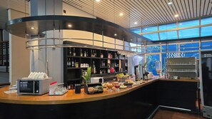 Un espace bar moderne doté d’un comptoir incurvé, d’étagères remplies de bouteilles et d’une variété de produits alimentaires et de boissons.