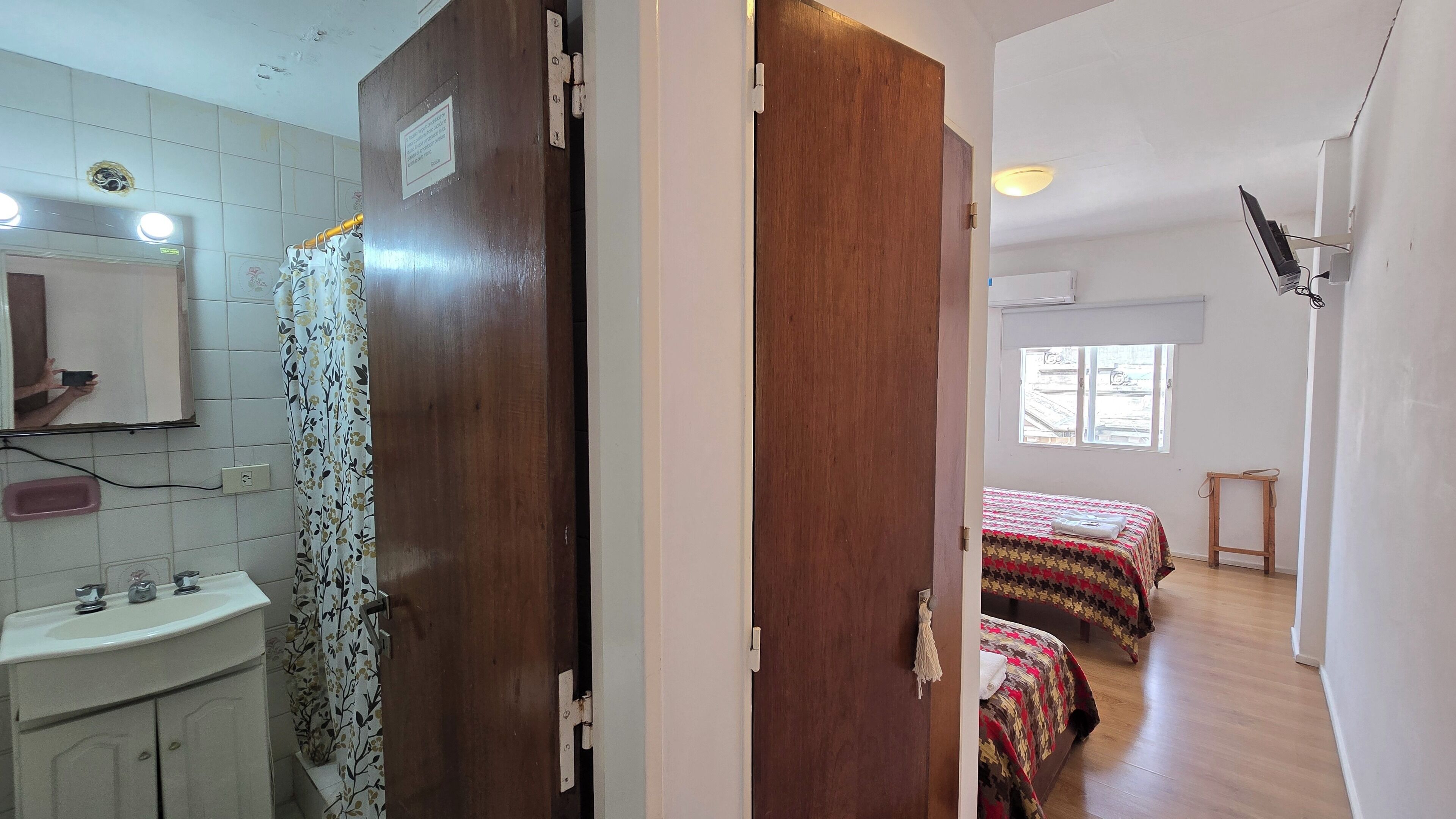 Una stanza con una porta in legno, uno specchio, un lavandino e un letto con copripiumino decorato.