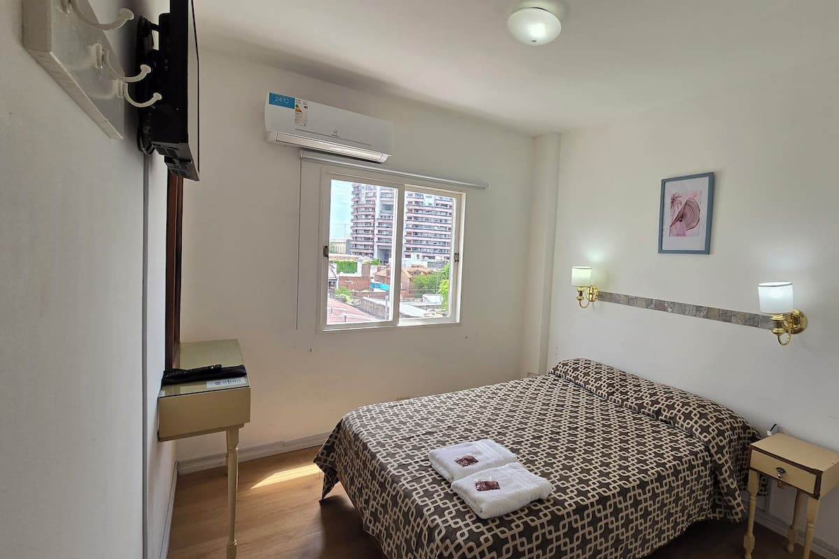 Ein Schlafzimmer mit einem Bett, einem Fenster, einem Nachttisch, einer Lampe und einer Wand-Klimaanlage.