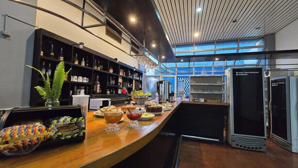 Un restaurant d’hôtel avec un comptoir en bois, des étagères remplies de bouteilles et une vue dégagée grâce à de grandes fenêtres.