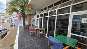 Une vue de l’extérieur d’un hôtel, avec des tables et des chaises en plein air, des palmiers et une vue sur la rue.