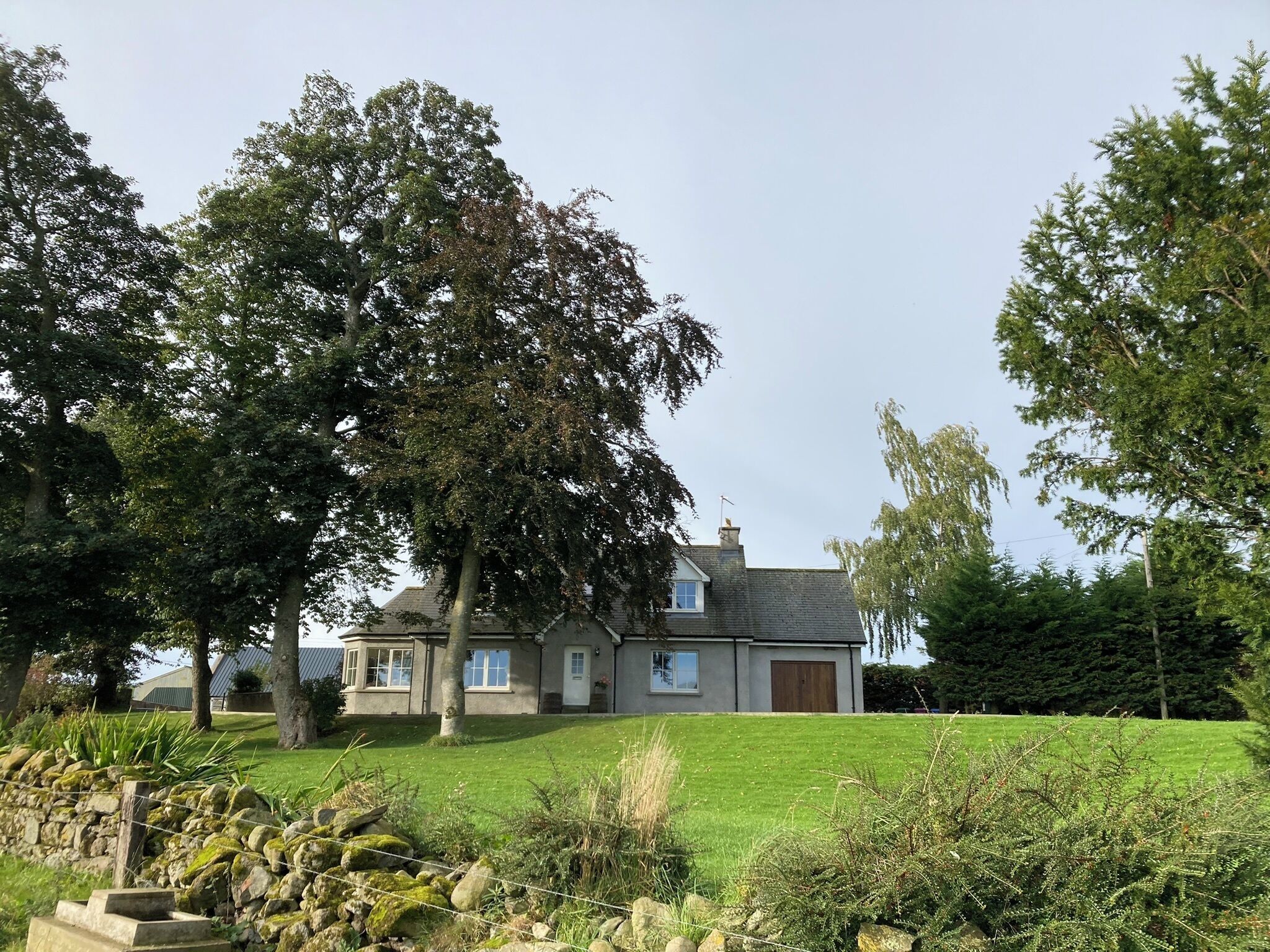A two-story house with a well-maintained lawn, a stone wall, and mature trees.