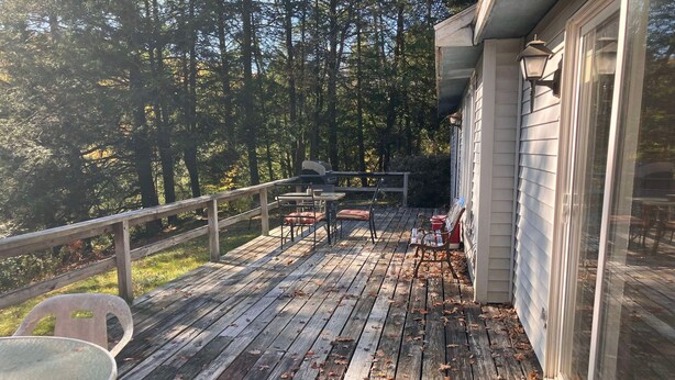 Una terraza de madera con sillas y una mesa, rodeada de árboles.