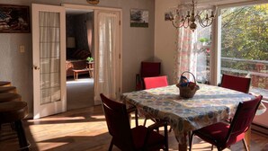 Un comedor con una mesa cubierta por un mantel estampado con motivos de hojas, rodeada de sillas rojas.