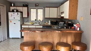 Una cocina con una isla de madera, taburetes de bar, un refrigerador, un microondas y un lavamanos.