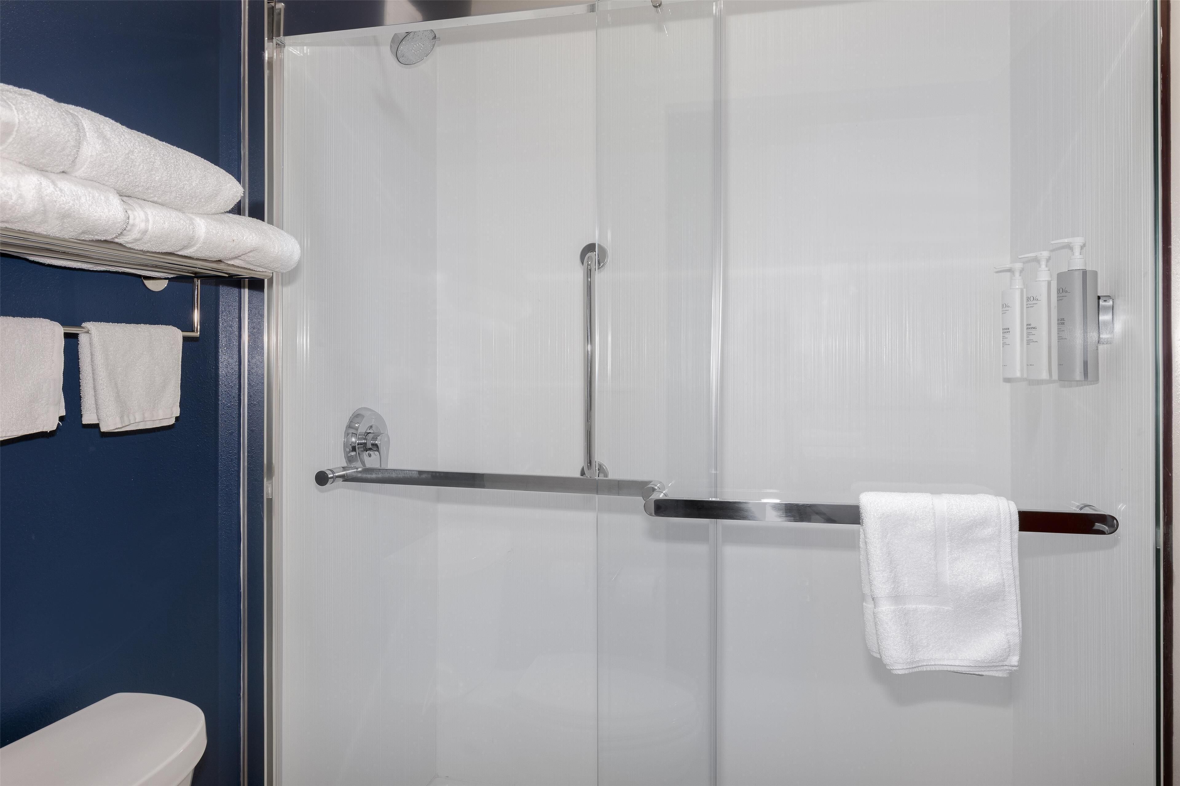 A bathroom with a glass shower enclosure, a towel rack with towels, and toiletries on the wall.