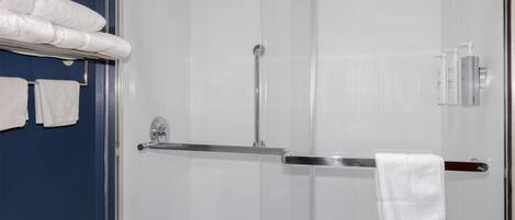 A bathroom with a glass shower enclosure, a towel rack with towels, and toiletries on the wall.