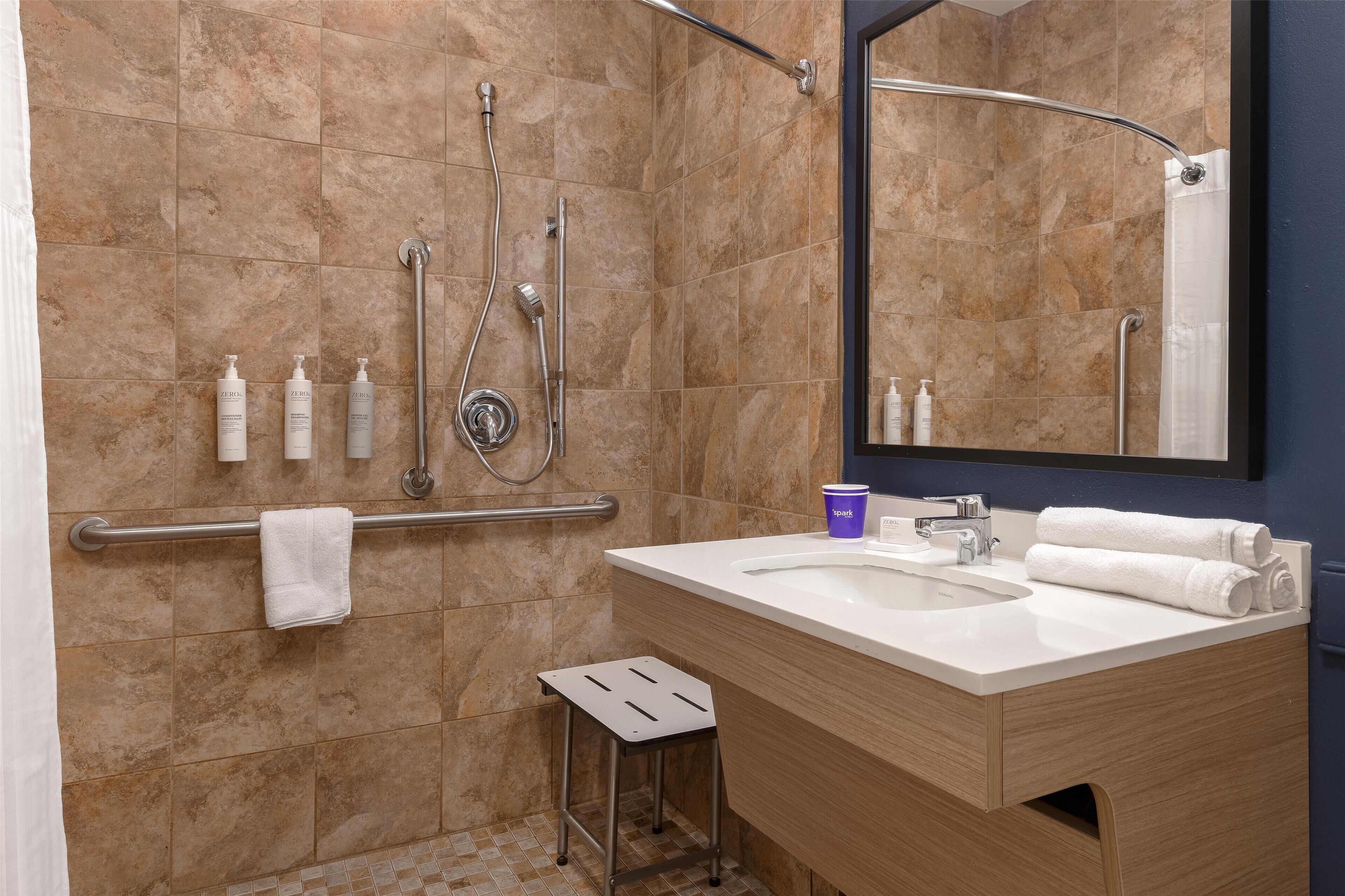 Un baño moderno con ducha de azulejos color beige, un lavamanos blanco y un mueble de tocador de madera.