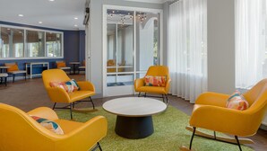 Un'area lounge moderna con poltrone gialle, un tavolo rotondo e ampie finestre con tende leggere.