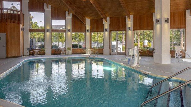 Una piscina interna con travi in legno, ampie finestre e zone relax all'aperto.