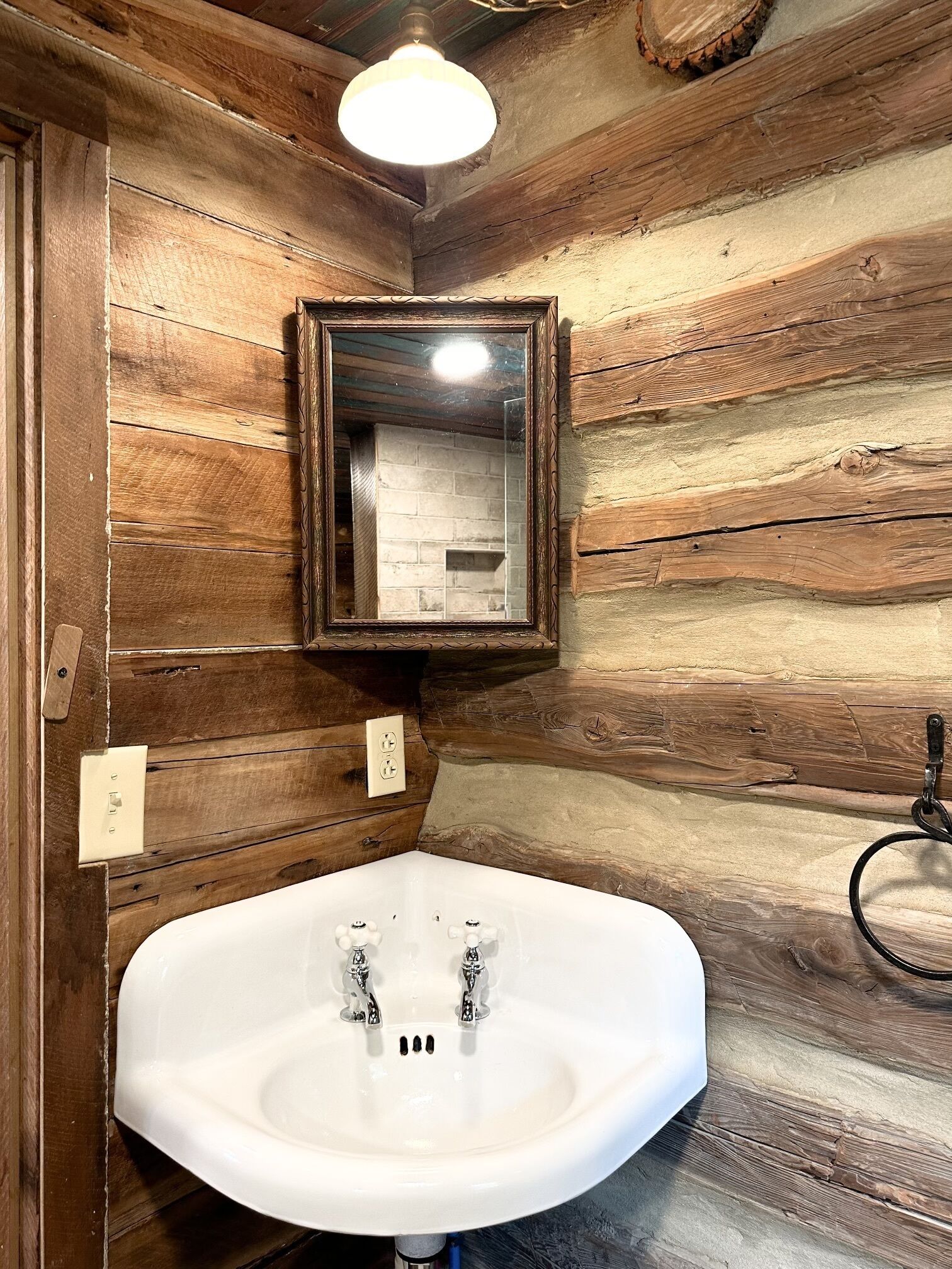 Une salle de bain rustique avec un mur en bois, un lavabo blanc et un miroir.