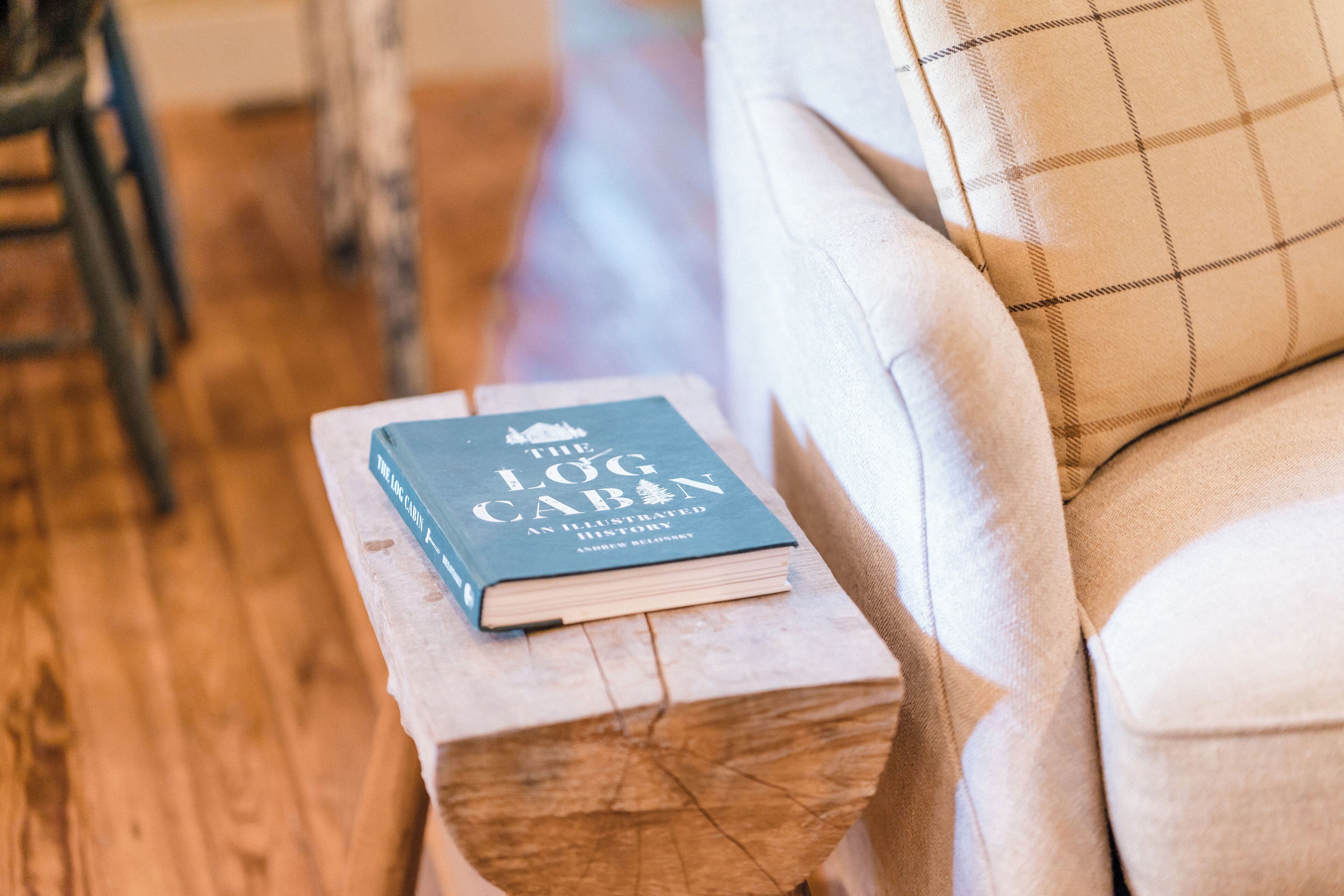 Un libro intitolato "The Log Cabin" su uno sgabello di legno vicino a un divano.
