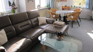 Ein modernes Wohnzimmer mit einer Ledersofa, einem Glastisch, Korbstühlen, einem Esstisch und Kunstwerken an den Wänden.