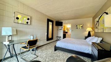Une chambre d’hôtel avec un lit, un bureau et une chaise, une télévision et une salle de bain visible à travers une porte ouverte.