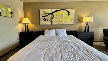 Une chambre d’hôtel avec un grand lit, deux tables de chevet avec des lampes, un tableau abstrait accroché au mur et un sol recouvert de moquette.