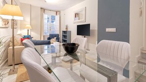 A modern living room with a glass coffee table, white sofas, a blue armchair, and a TV mounted on the wall. - Genteel Home San Isidoro II (Seville)