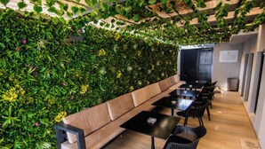A modern lounge area with a long sofa, black tables, and chairs, surrounded by a lush green wall with plants. - Bon Hotel Boutique Garki 2 (Abuja)