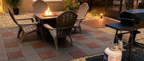 An outdoor patio with a fire pit, seating, and a grill.