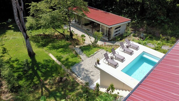 Una casa moderna con techo rojo, piscina y un patio con sillones de descanso.