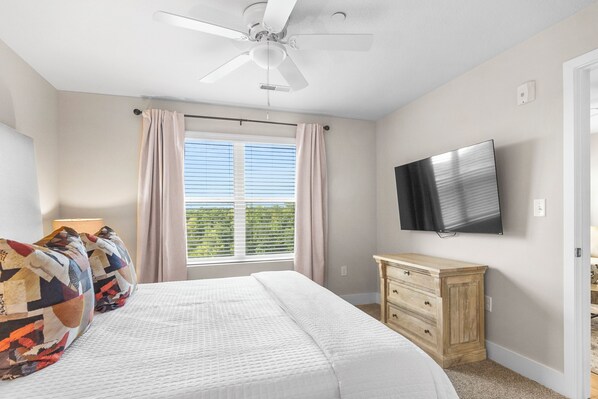 Ein Schlafzimmer mit Bett, Deckenventilator, Fernseher, Fenster mit Vorhängen und einem Holzkoffer.